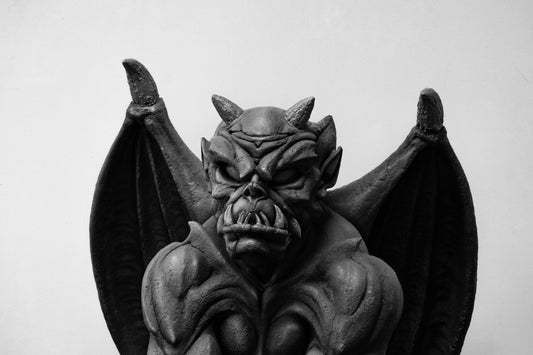 Close up image of the face of a black goyle on a white/grey background. Scary and imposing, its teeth gnashing and eyes glaring..