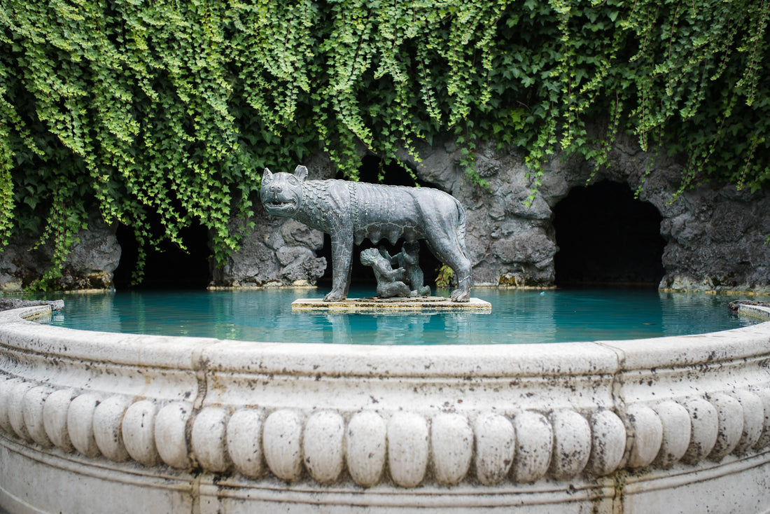 "Bronze statue of Romulus and Remus with the she-wolf in a decorative fountain surrounded by ivy and stone grotto, outdoor garden sculpture