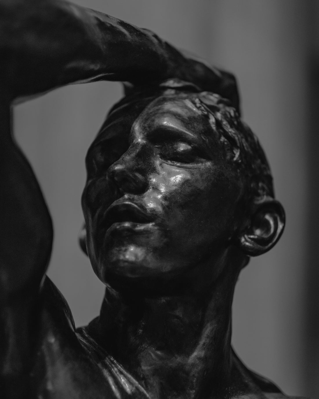 An all black sculpture, black and white background. The sculptures hand is on his hand, combing his hard back. A look of relief is on his face.