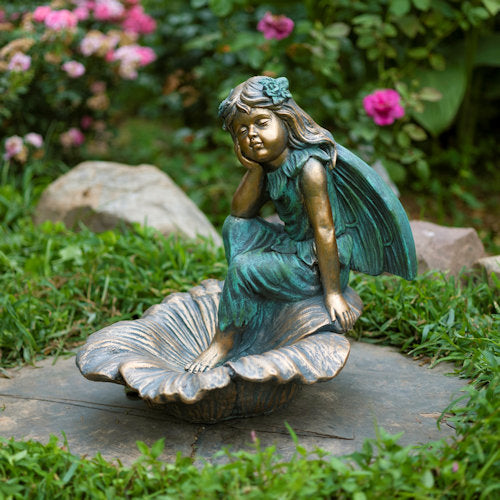 Garden statue of a fairy sitting on a shell with flowers in the background