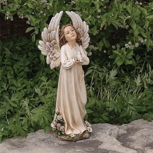 Angel statue with wings spread, holding flowers, standing on a rock with greenery in the background