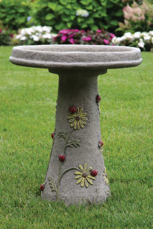 Decorative stone bird bath with floral designs on a grassy background with high relief ladybugs