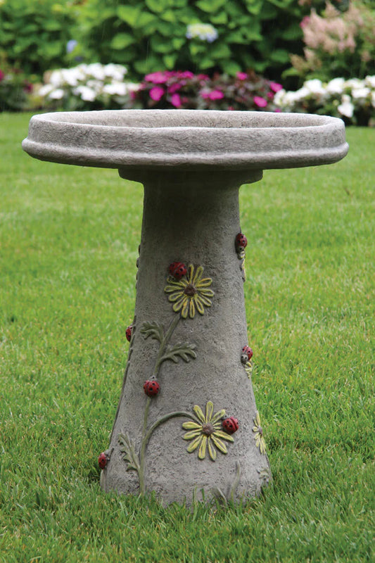 Decorative stone bird bath with floral designs on a grassy background with high relief ladybugs