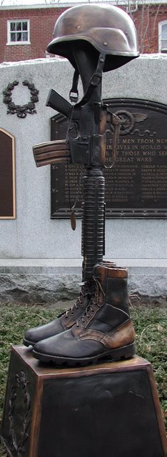 Statue of a helmet, rifle, and boots on a pedestal in front of a memorial plaque War Memorial for Military
