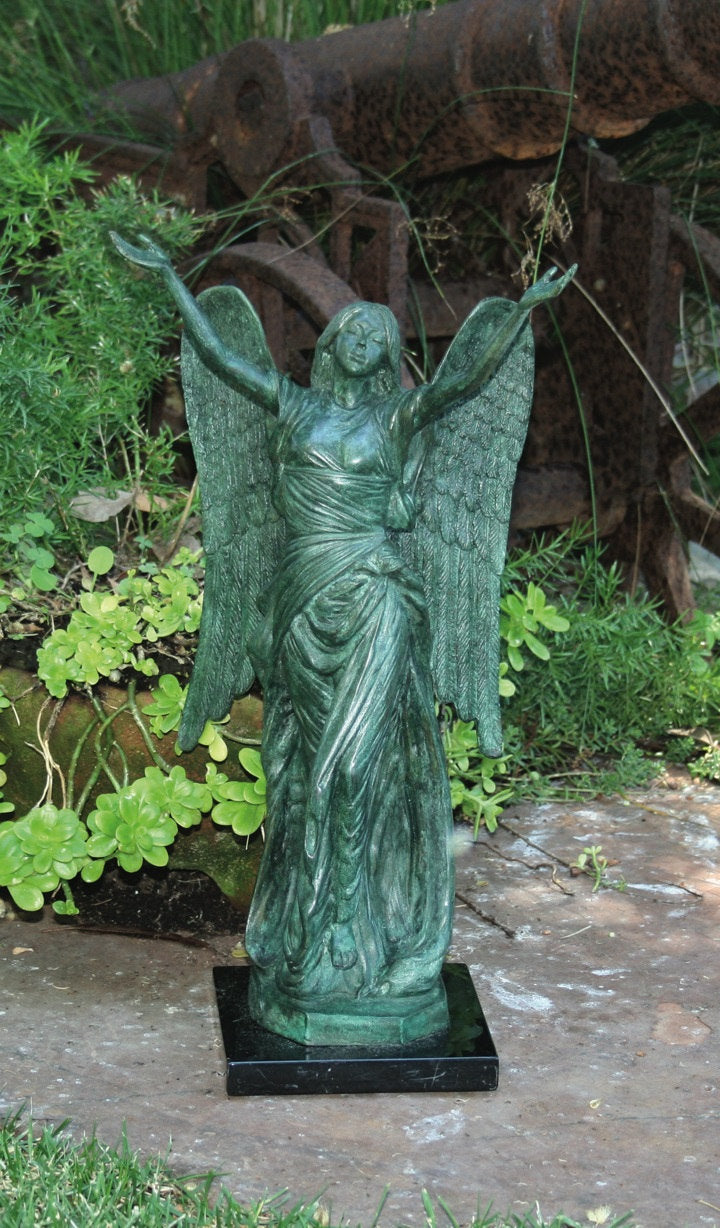 Statue of an angel with outstretched wings on a stone surface with greenery in the background