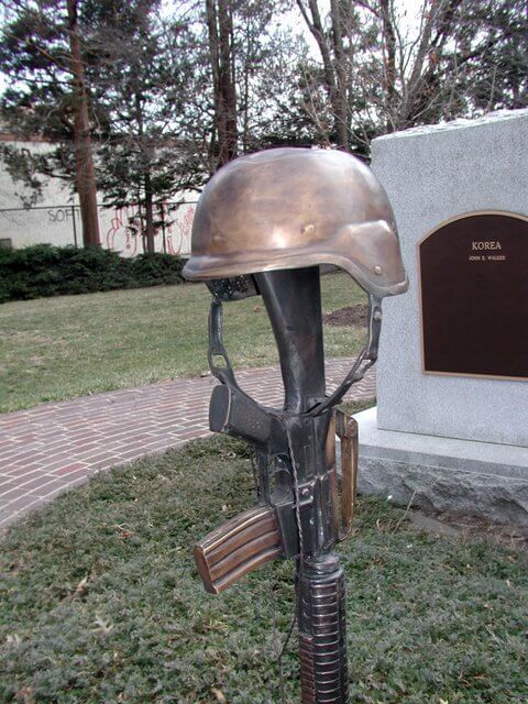 Bronze sculpture of a helmet and rifle in front of a stone monument with 'Korea' engraved.
