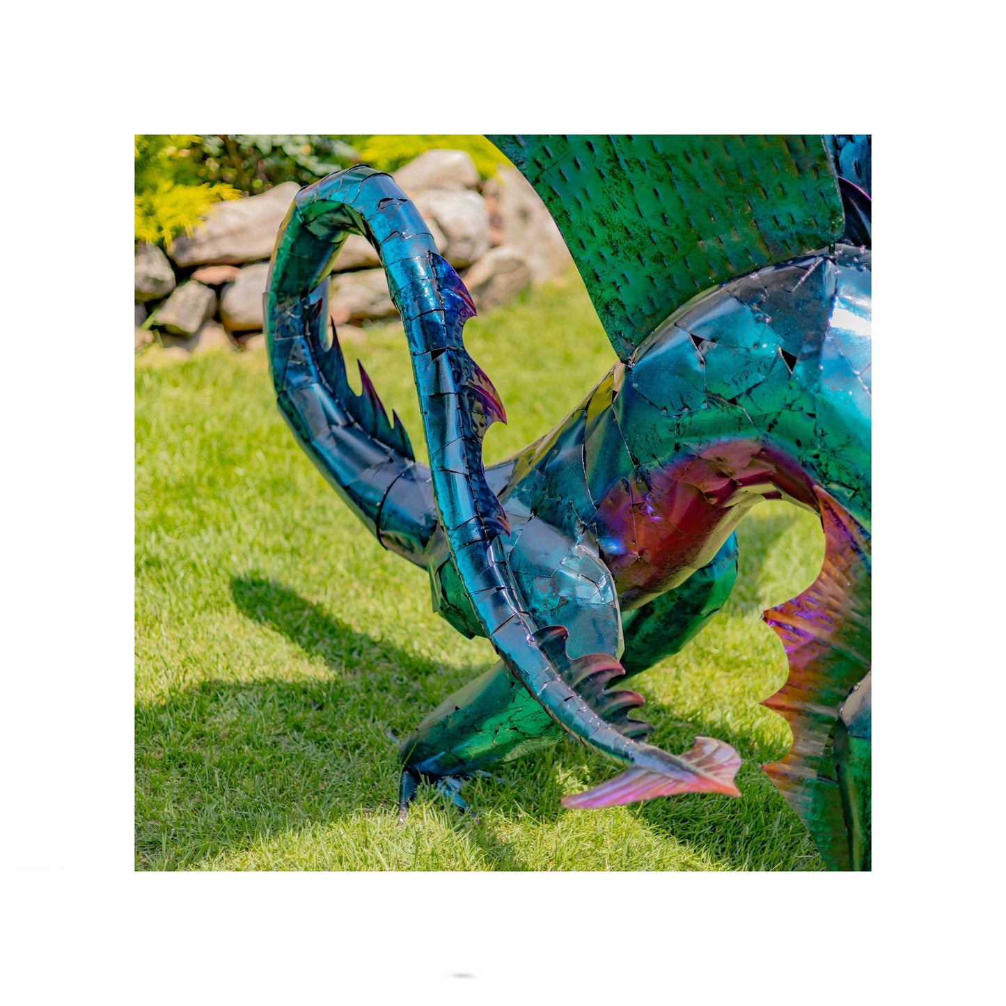 Metallic dragon sculpture on grass with stone wall in background close up of tail