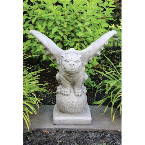 Stone gargoyle statue in a garden setting with greenery.