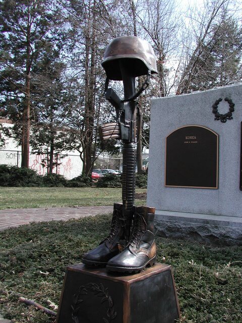 Statue of a helmet and boots on a pedestal with a plaque in the background