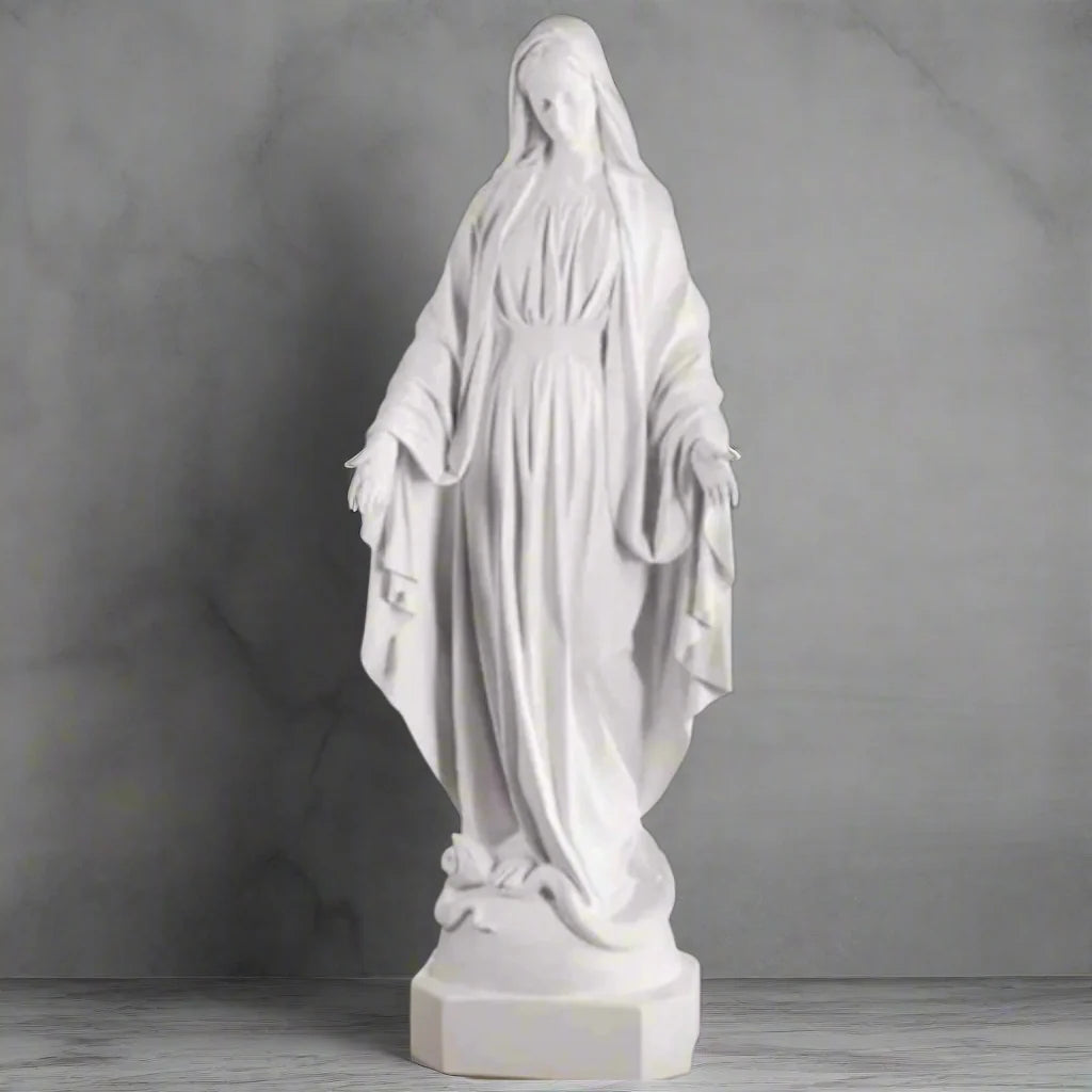 Bonded marble Virgin Mary statue, life-size and serene, shown outdoors with flowers and greenery surrounding a memorial-style base