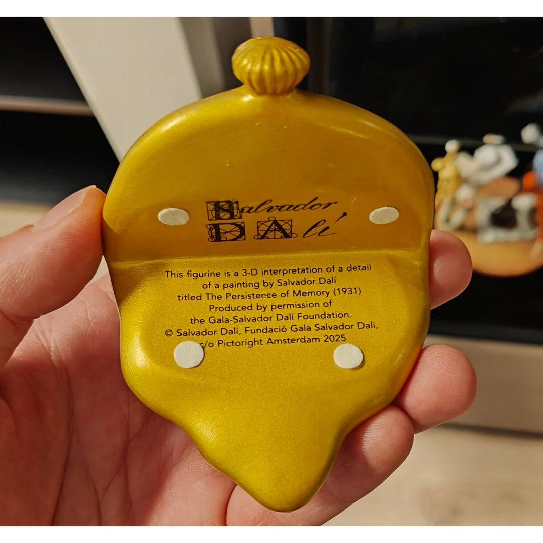 Yellow Salvador Dali figurine held in a hand with branding and text.