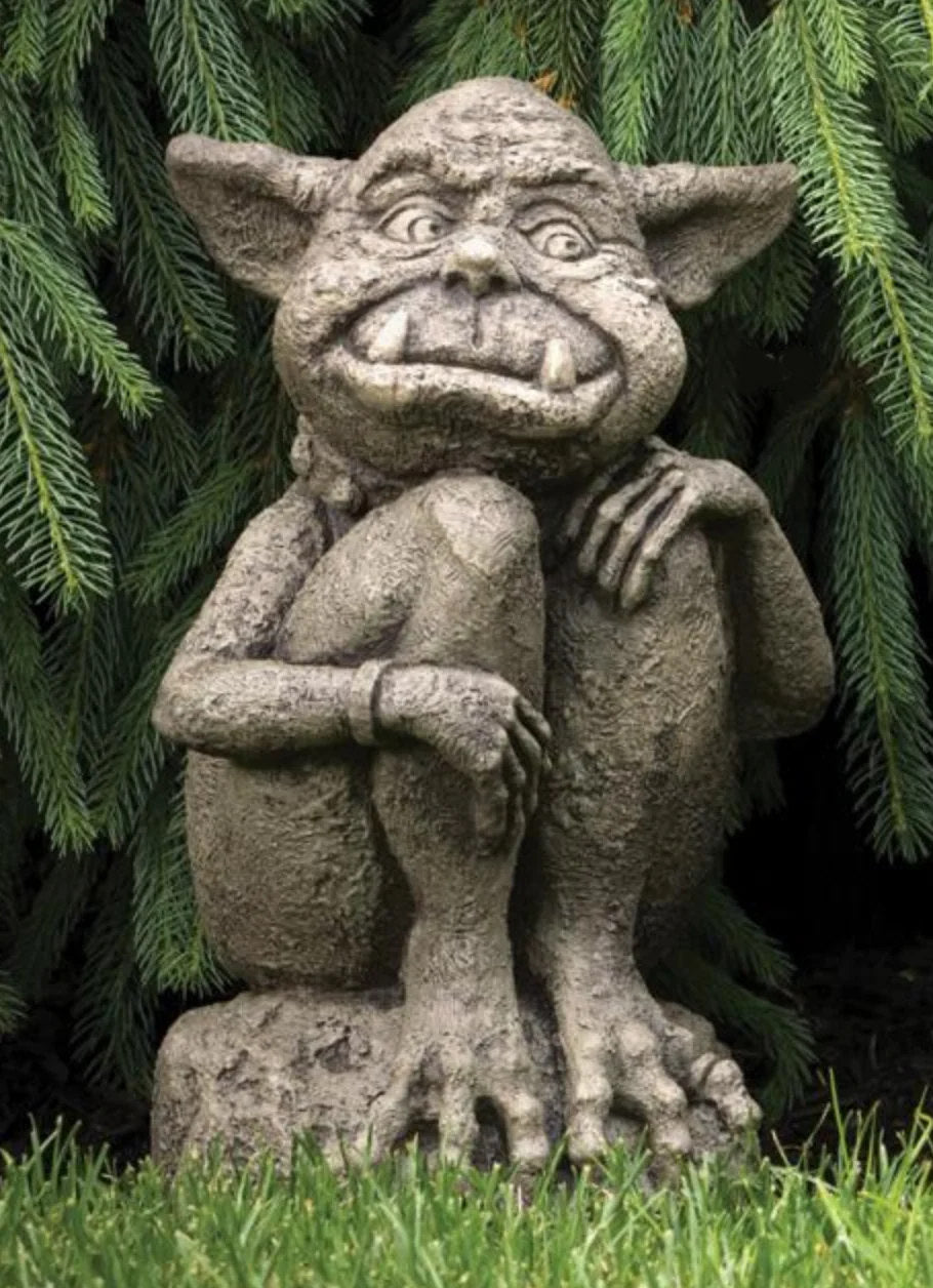 Stone gargoyle statue against a green leafy background