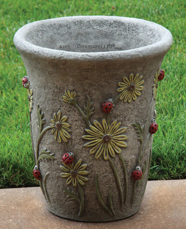 Decorative stone planter with floral and ladybug designs on a grass background