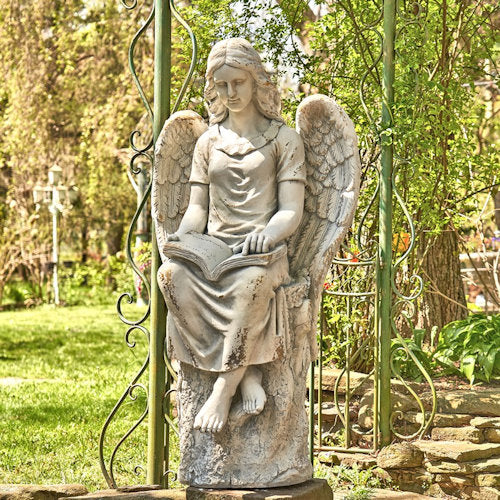 Statue of an angel holding a book in a garden setting