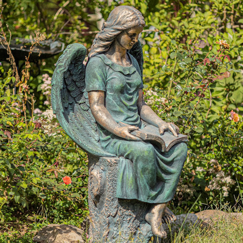 Statue of an angel reading a book in a garden setting