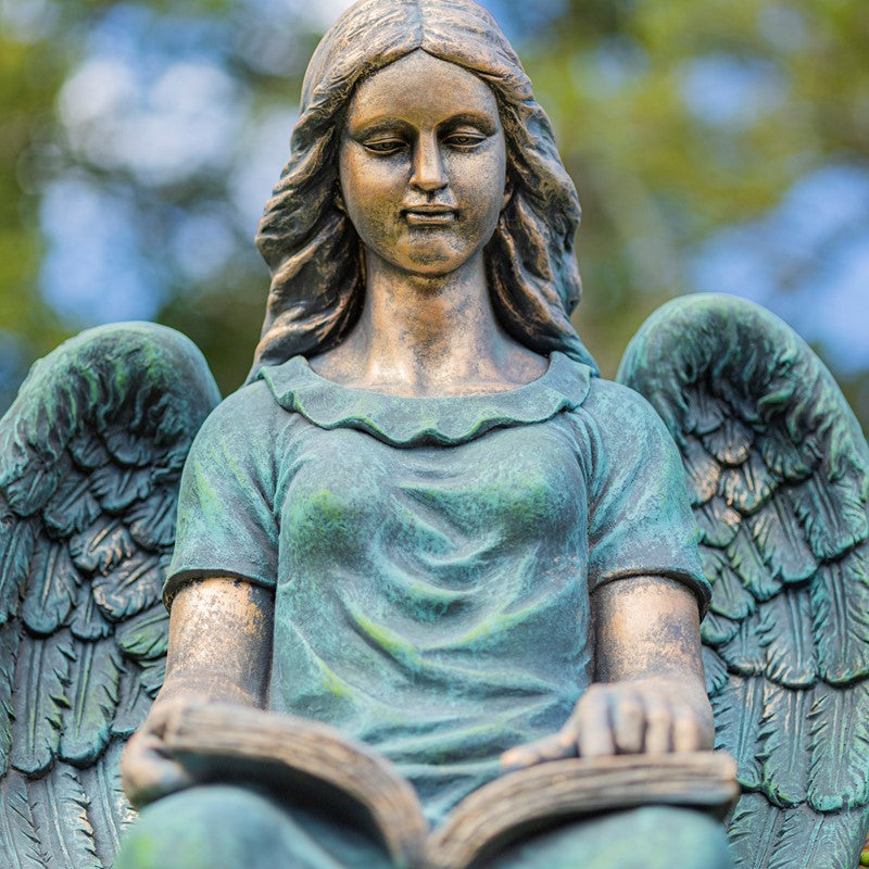 Bronze statue of an angel with wings spread, sitting and holding a book.