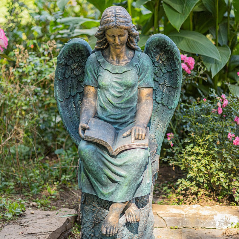 Statue of an angel holding a book in a garden setting