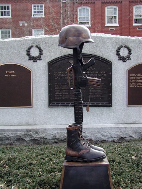 Memorial sculpture with helmet, boots, and rifle in front of a brick building with plaques.