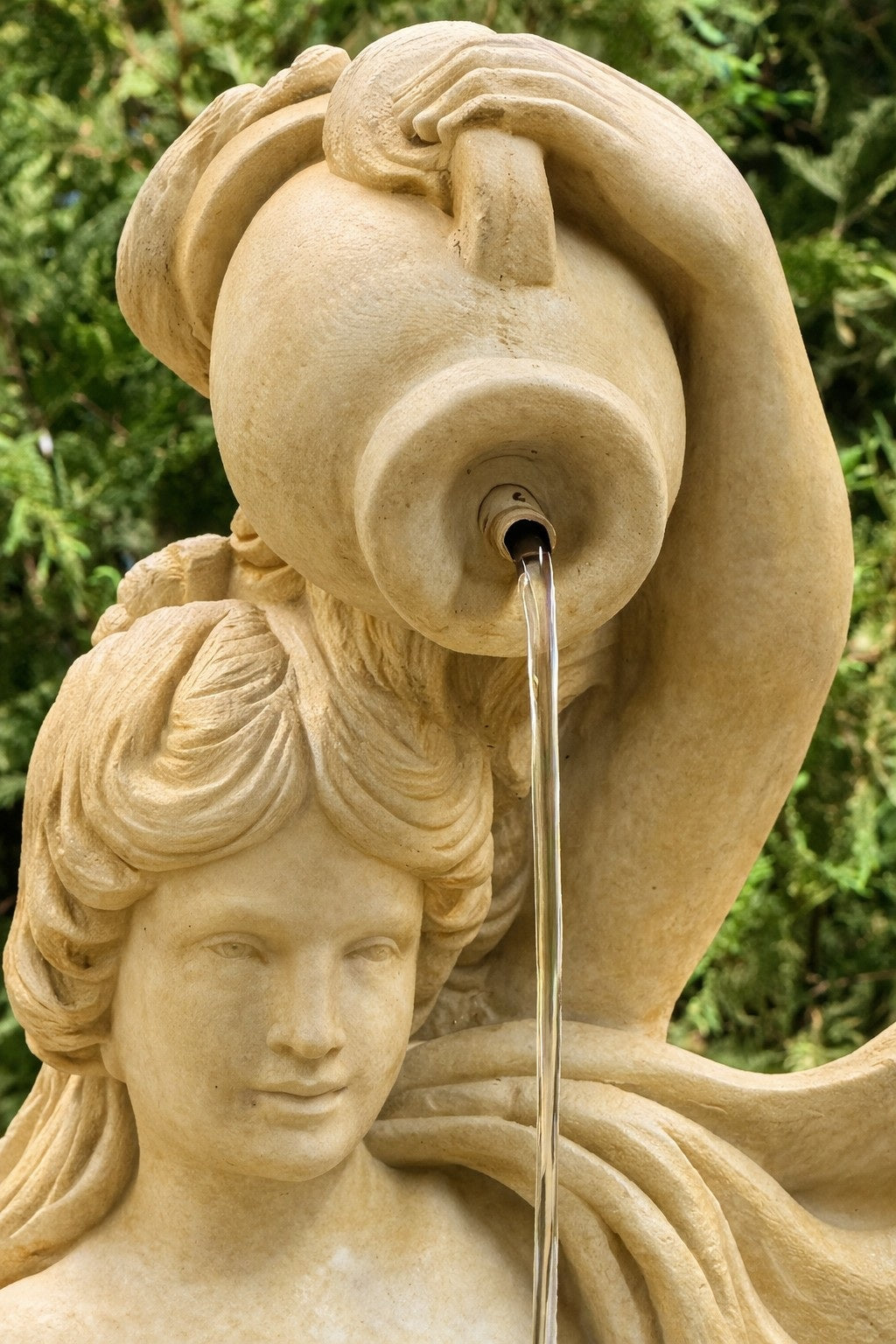 Stone sculpture of a woman with flowing hair and a vase, with water spouting from it, against a green background.