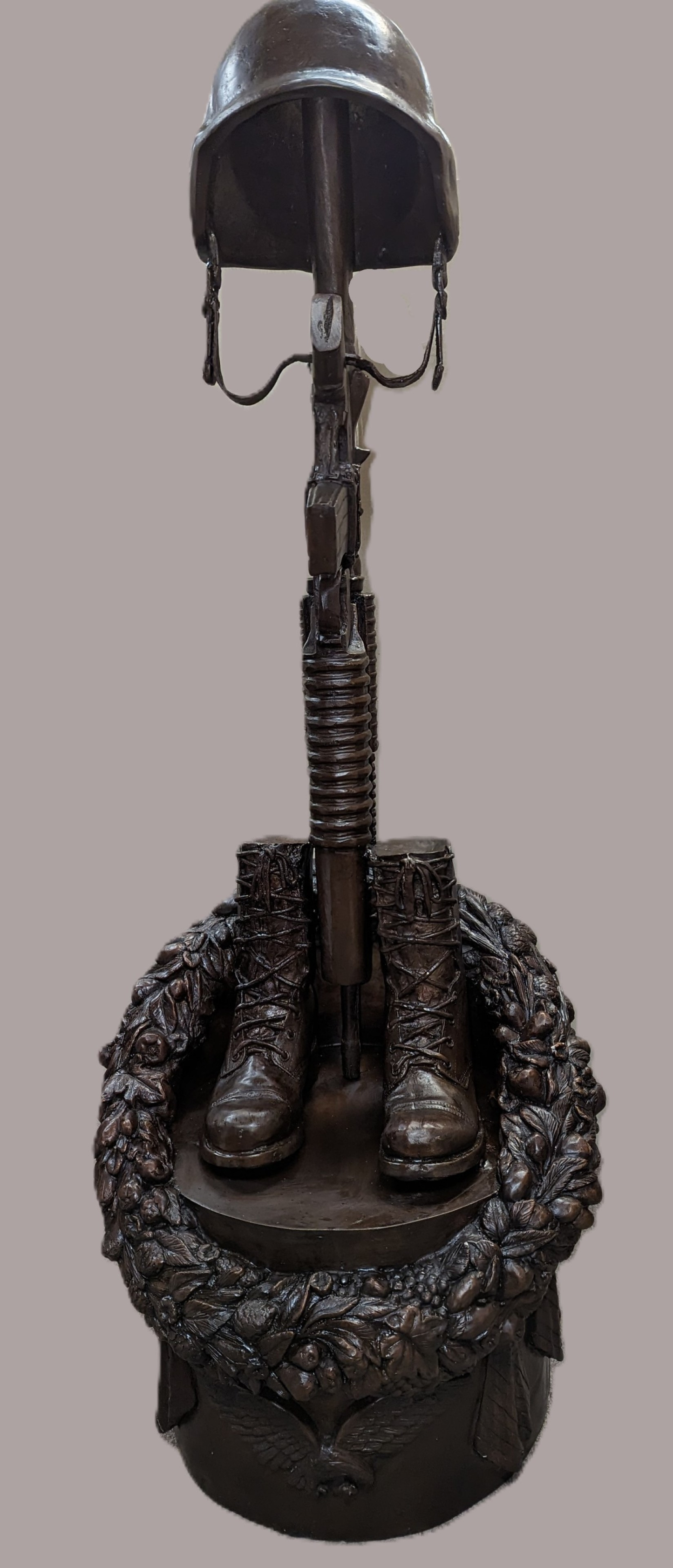 Bronze sculpture of a military figure with helmet, boots, and rifle on a gray background
