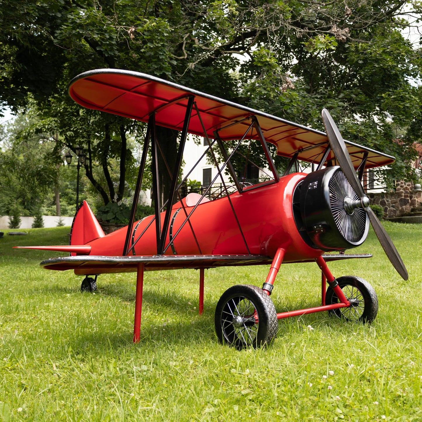 Red biplane model on grass with trees in the background close up of propeller