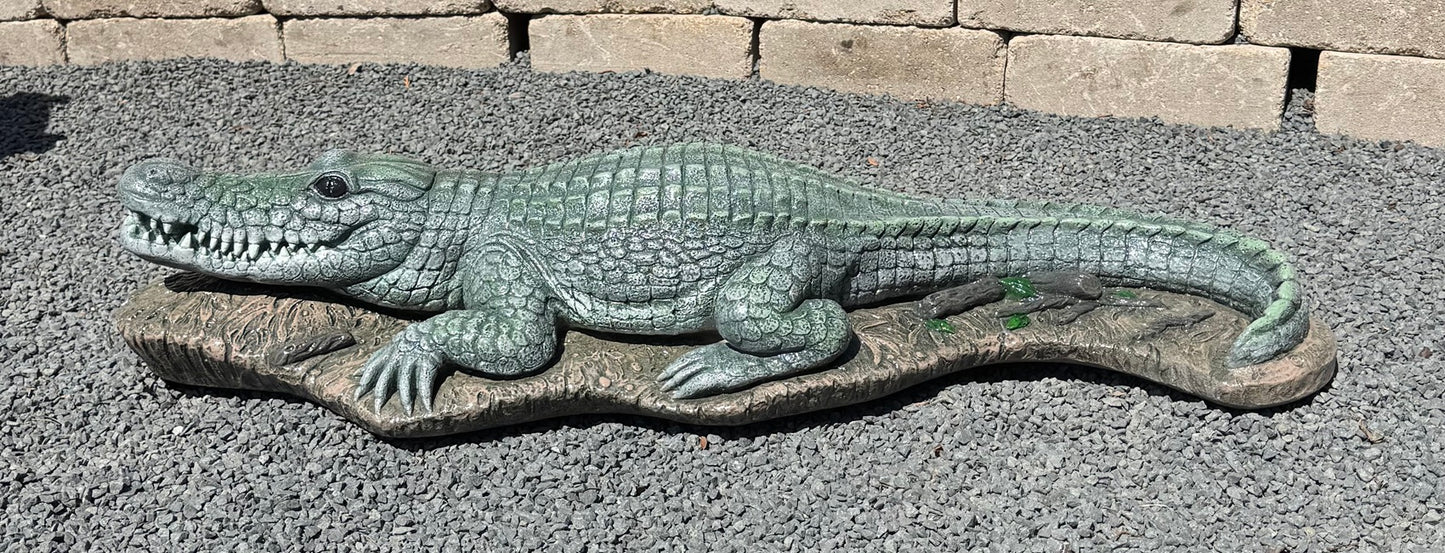 Decorative alligator statue on a gravel surface with a stone wall background
