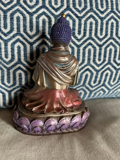 The back of the Buddha statue with purple hair and base against a patterned fabric background