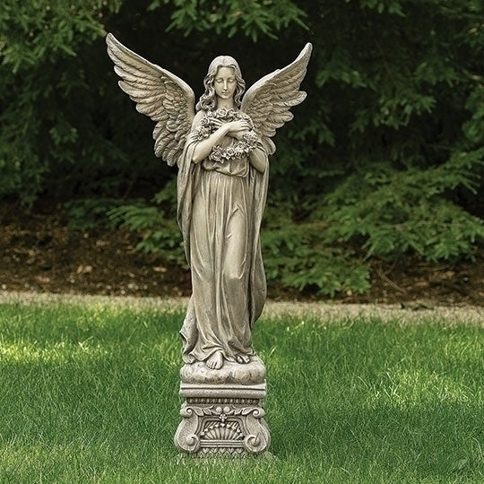 Statue of an angel holding flowers on a grassy area with trees in the background