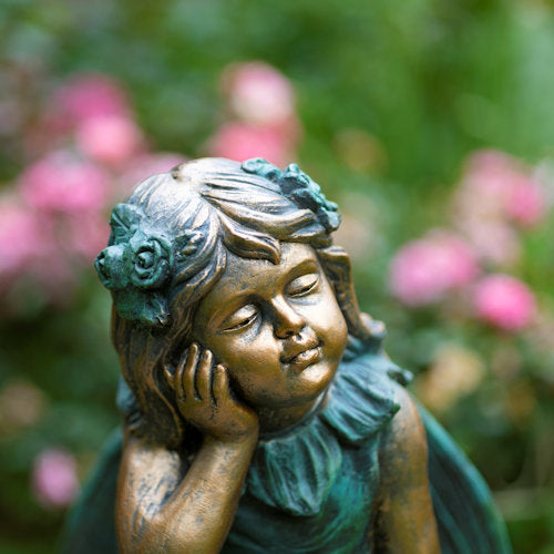 Bronze statue of a girl with flowers in her hair against a blurred floral background