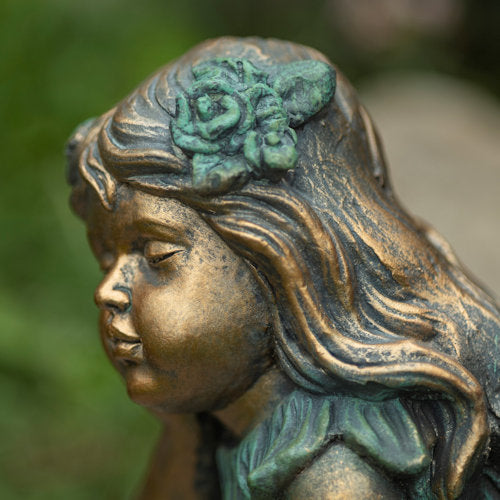 Bronze statue of a woman with a flower in her hair against a blurred natural background