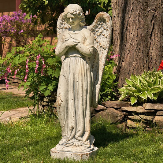 Statue of an angel in a garden setting with plants and flowers.