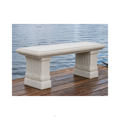 A rectangular outdoor bench made of light beige stone or concrete, featuring fluted column-style legs, shown on a wooden dock with water in the background.