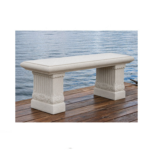 A rectangular outdoor bench made of light beige stone or concrete, featuring fluted column-style legs, shown on a wooden dock with water in the background.