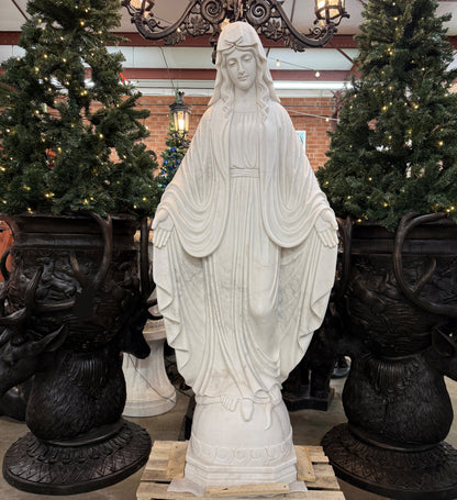 White marble statue of a religious figure in a decorative setting with Christmas trees and black urns.