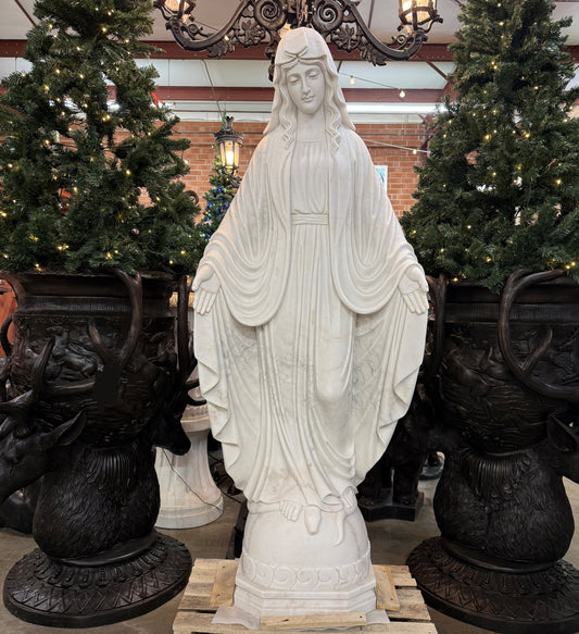White marble statue of a religious figure in a decorative setting with Christmas trees and black urns.