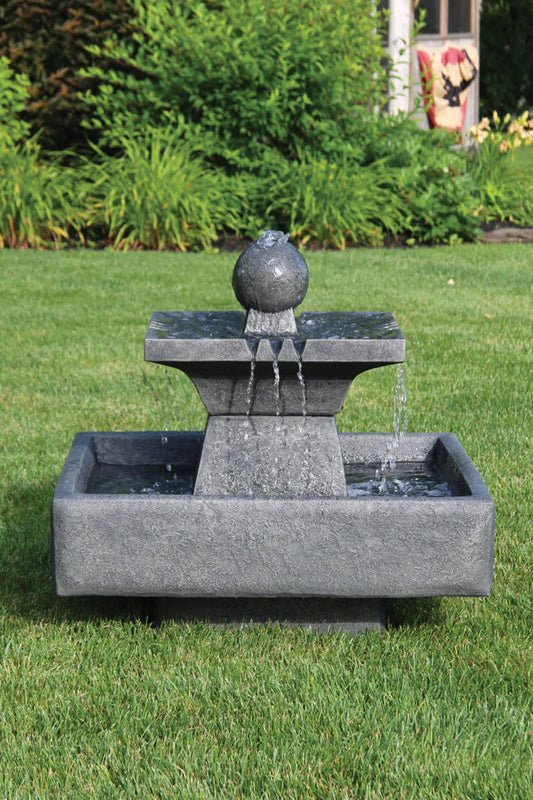 Gray stone fountain with water feature on a grassy lawn