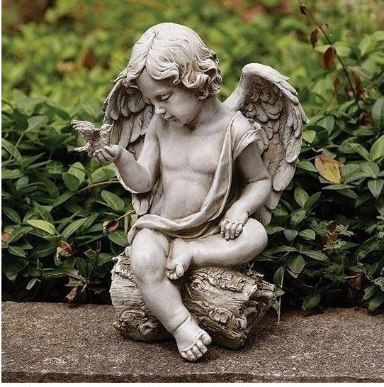 Statue of an angel holding a dove bird in a garden setting sitting on log