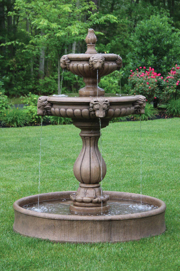 lion head Three-tiered stone fountain in a garden setting with green grass and trees.