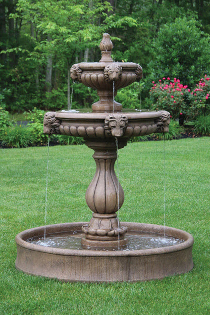 lion head Three-tiered stone fountain in a garden setting with green grass and trees.