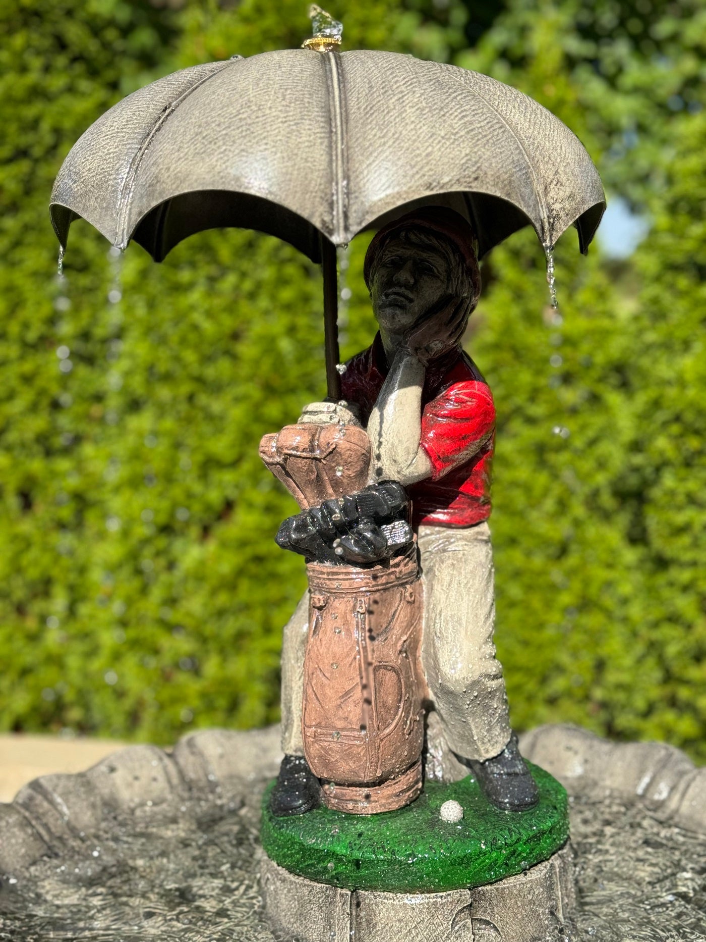 Statue of a golfer with an umbrella on a green base against a blurred natural background
