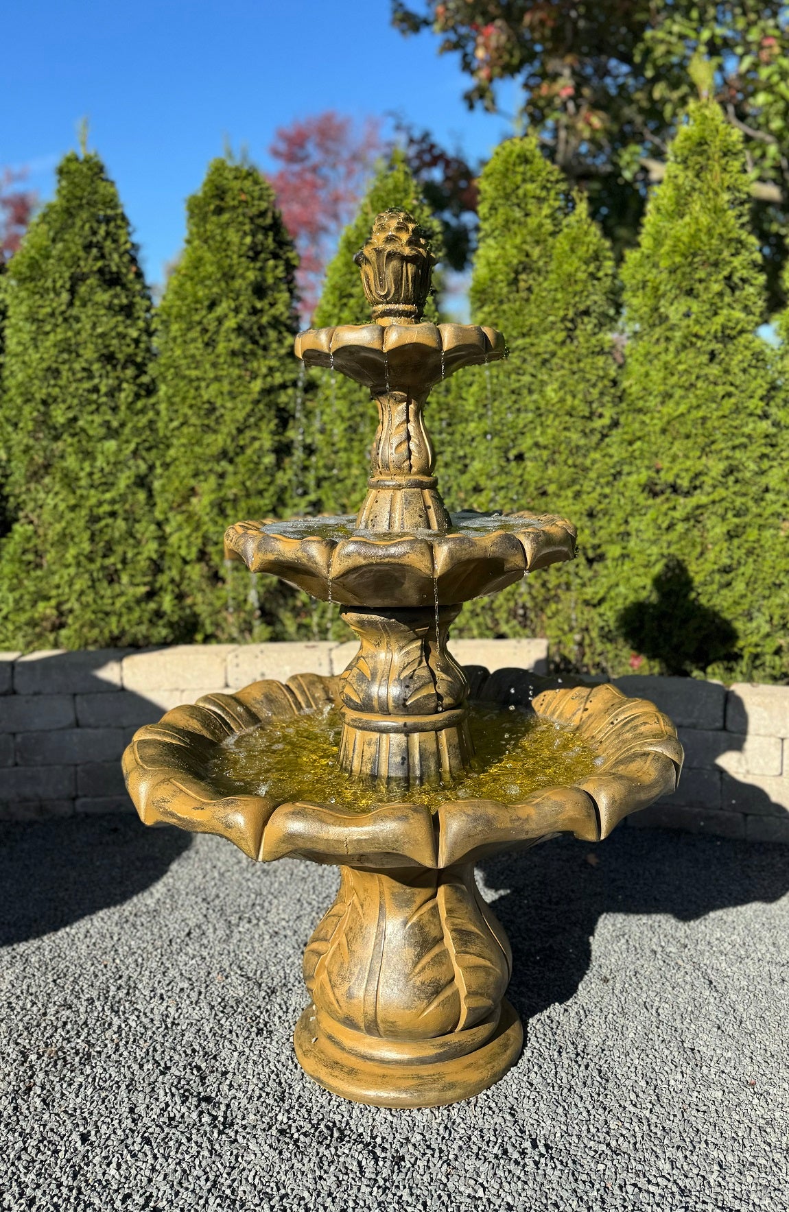 Three-tiered bronze fountain in a garden setting with trees in the background