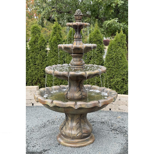 Three-tiered stone fountain with water flowing in a garden setting with pineapple finial top spouting