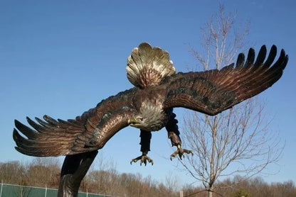 A large eagle sculpture with wings spread wide, shown outdoors against a clear blue sky and bare trees.