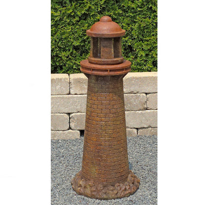A decorative lighthouse garden statue with a textured brick pattern in rust-brown and terracotta tones, shown standing on gravel in front of a stone wall and green hedge.