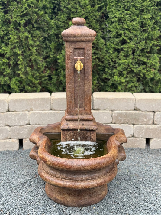 Decorative stone water fountain with a flowing water feature against a stone wall and greenery background.