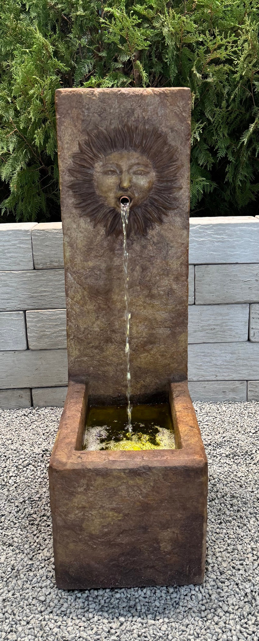 Decorative stone water fountain with sun face spouting water design in a garden setting