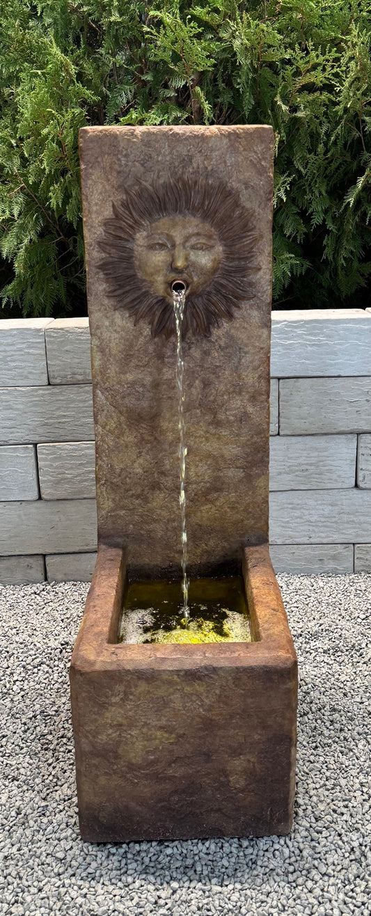 Decorative stone water fountain with sun face spouting water design in a garden setting