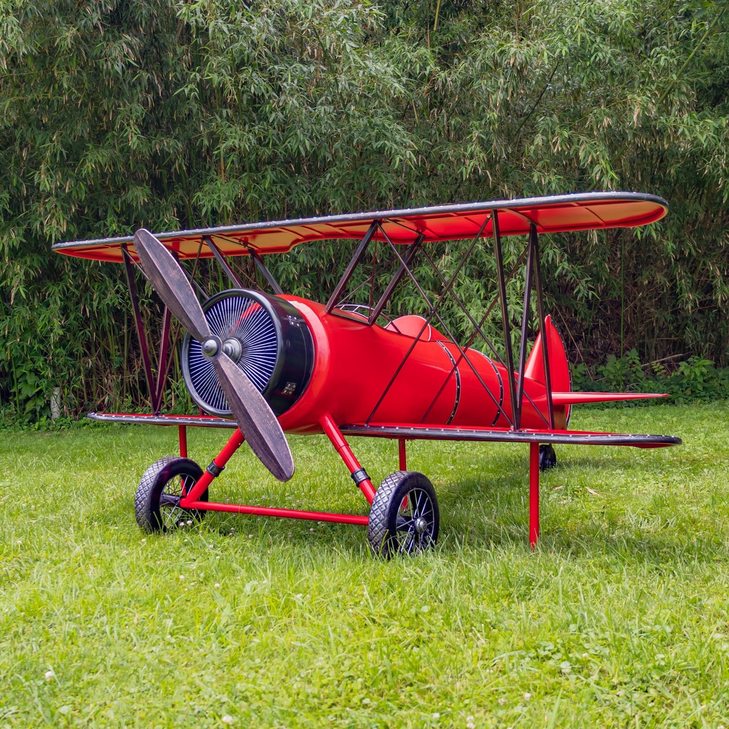 Red biplane model on grass with trees in the background