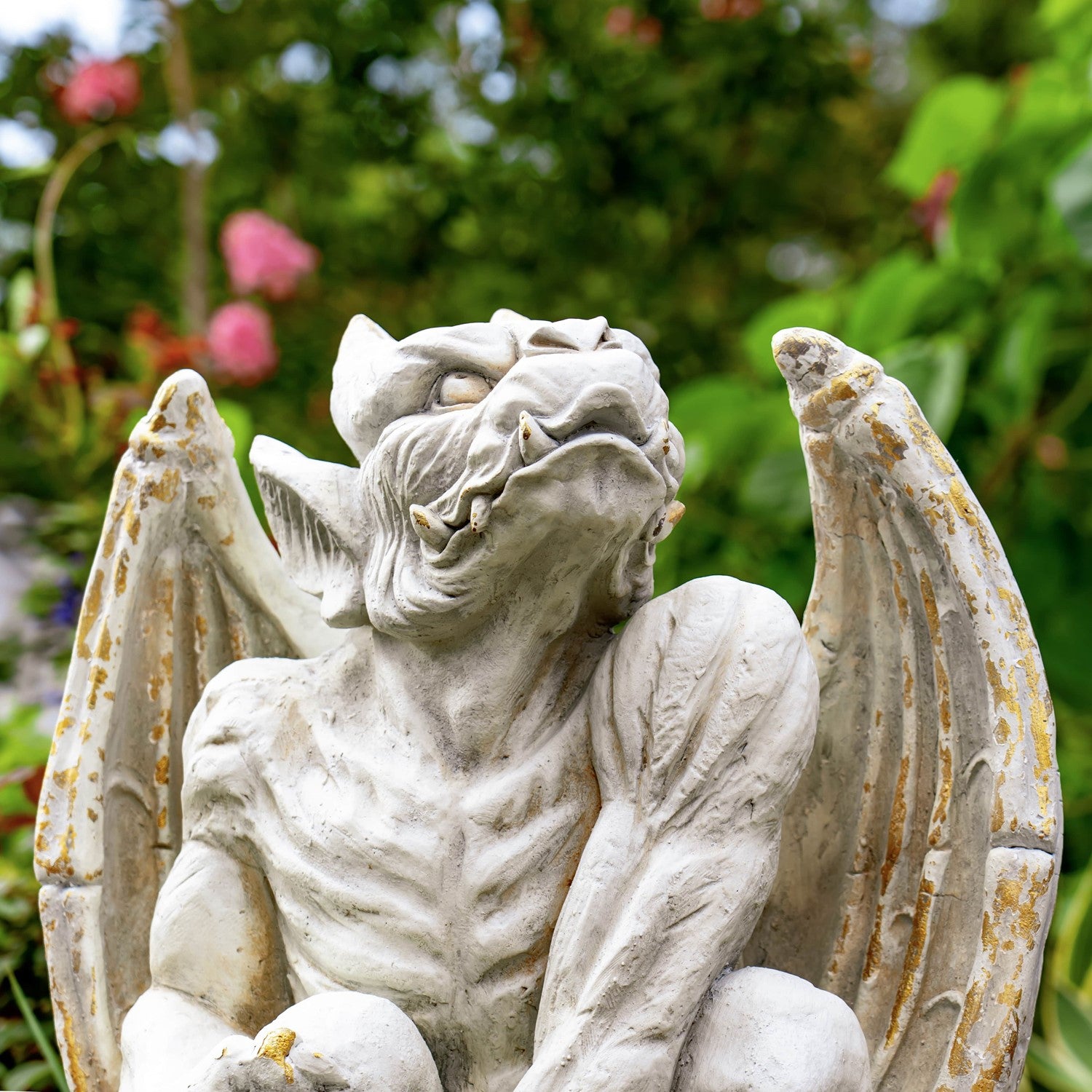 Stone gargoyle statue with wings in a garden setting