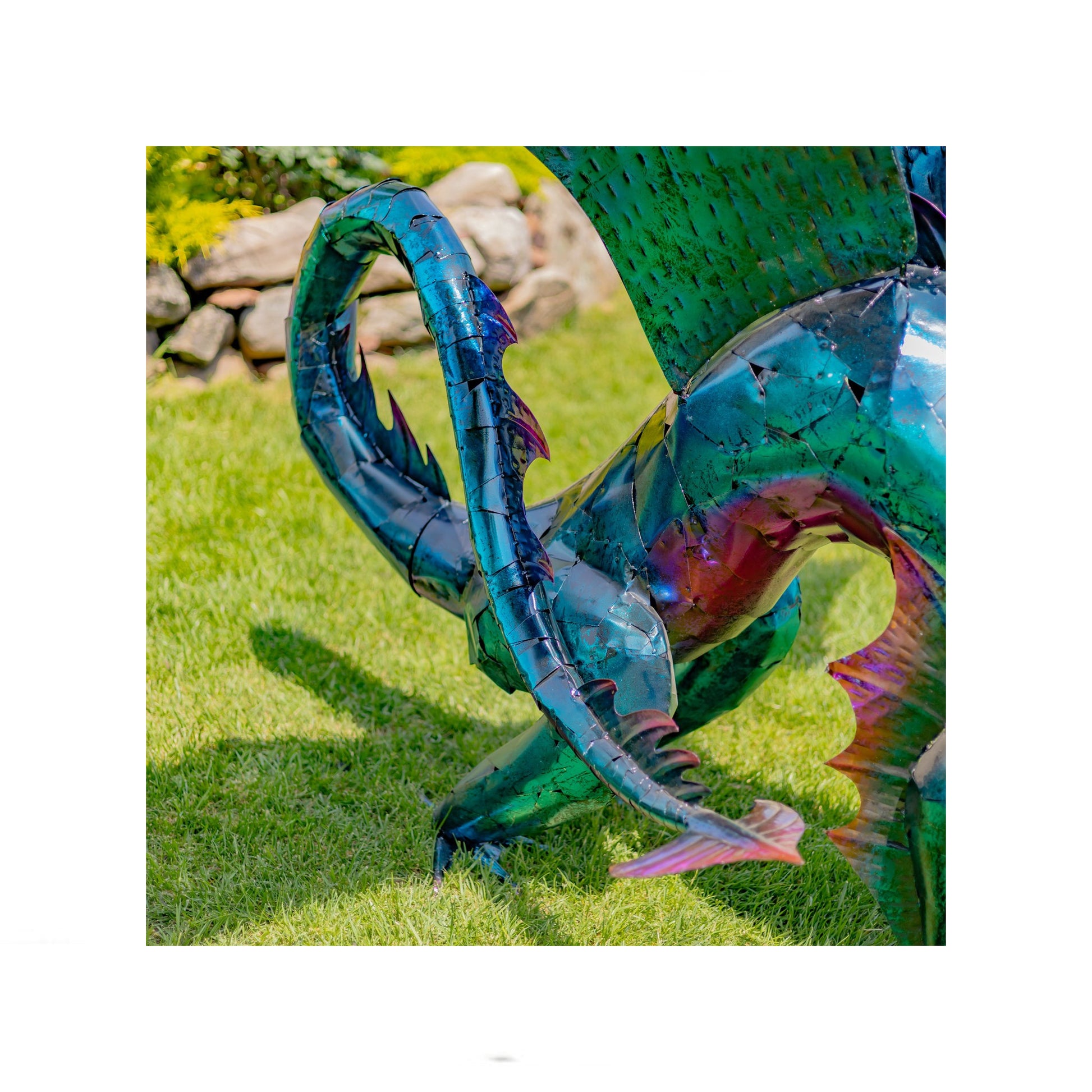 Metallic dragon sculpture on grass with stone wall in background close up of tail